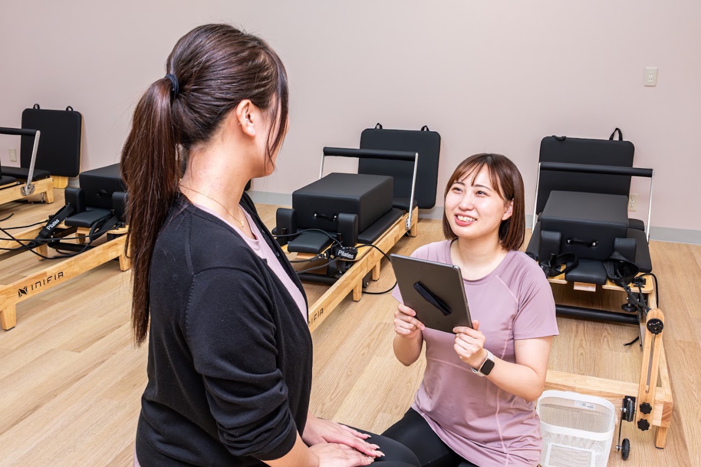 cocoro Pilates 沼津駅前店で、タブレットを持った指導者がお客様と向き合って話している様子。